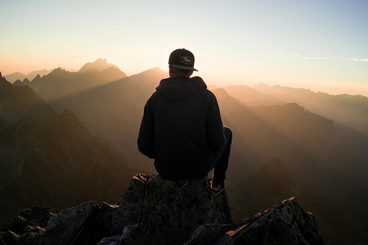 CBD Öl Wirkung. Foto eines Mannes, der auf einer Bergspitze sitzt bei Sonnenuntergang.