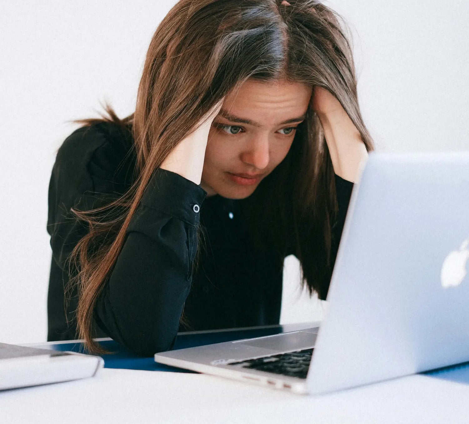 Eine Frau, die am Arbeitsplatz sitzt und sehr gestresst wirkt. Sie fasst sich mit beiden Händen an die Schlefen.