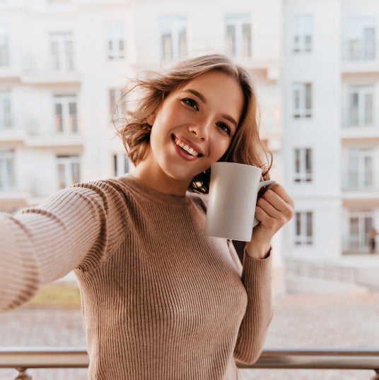 Eine Frau mit Kaffeetasse in der Hand macht ein Selfie.