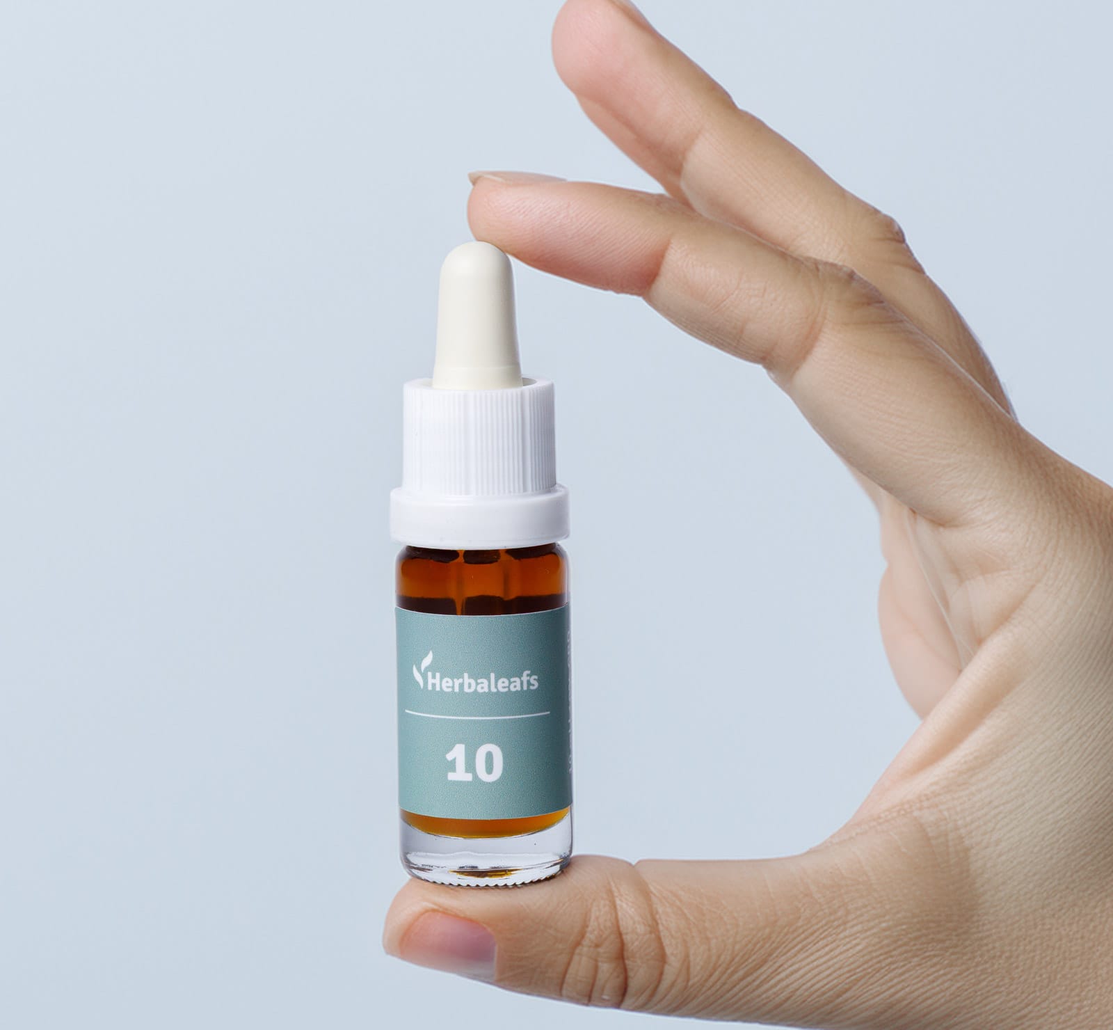 Hand, die eine Flasche 10 Prozent CBD-Öl zwischen Zeigefinger und Daumen hält.
