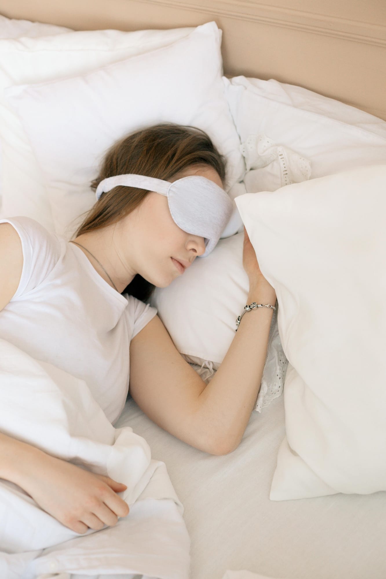 Eine Frau, die entspannt auf dem Bett liegt und mit einer Schlafmaske schläft.